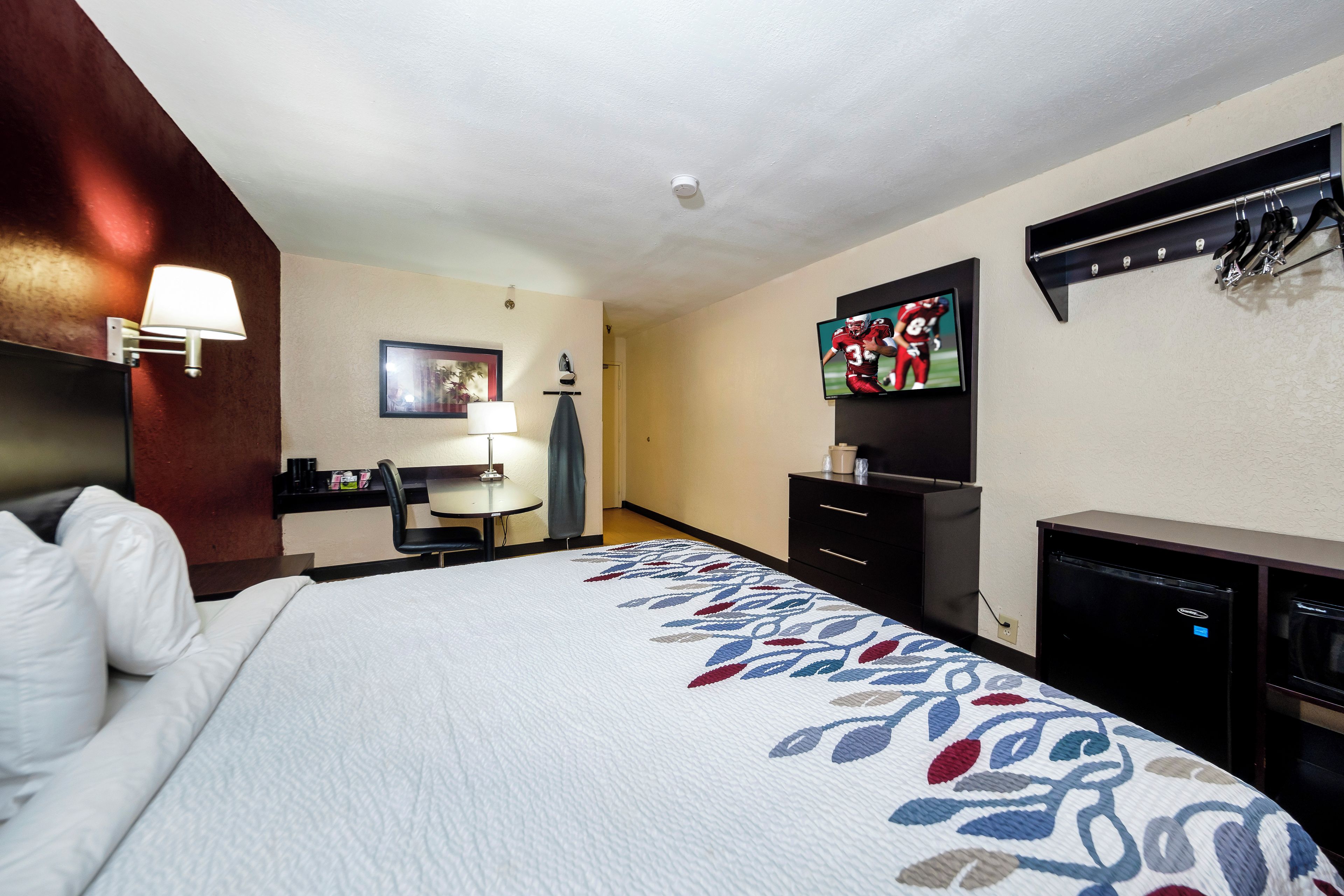 Ett hotellrum med en säng, ett skrivbord, en stol, en tv och en byrå.
