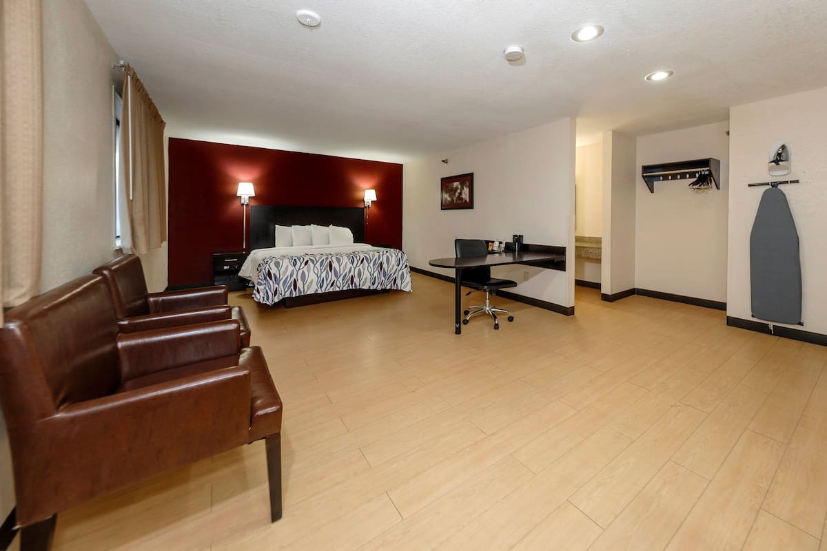 A hotel room with a bed, a desk, a chair, and a coat rack.