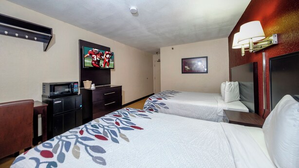 A hotel room with two beds, a television, a microwave, a desk, and a lamp. - Red Roof Inn Jacksonville - Cruise Port (Jacksonville)
