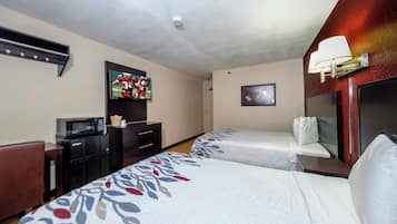 Ein Hotelzimmer mit zwei Betten, einem Fernseher, einer Mikrowelle, einem Schreibtisch und einer Lampe.