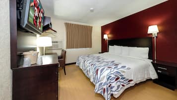 A hotel room with a bed, bedside lamps, a desk with a lamp, a television mounted on the wall, and a window with curtains.