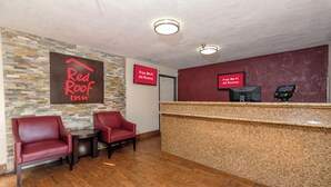 A Red Roof Inn reception area with a stone wall, two red chairs, a wooden reception desk, and two signs indicating free Wi-Fi in all rooms. - Red Roof Inn Jacksonville - Cruise Port (Jacksonville)