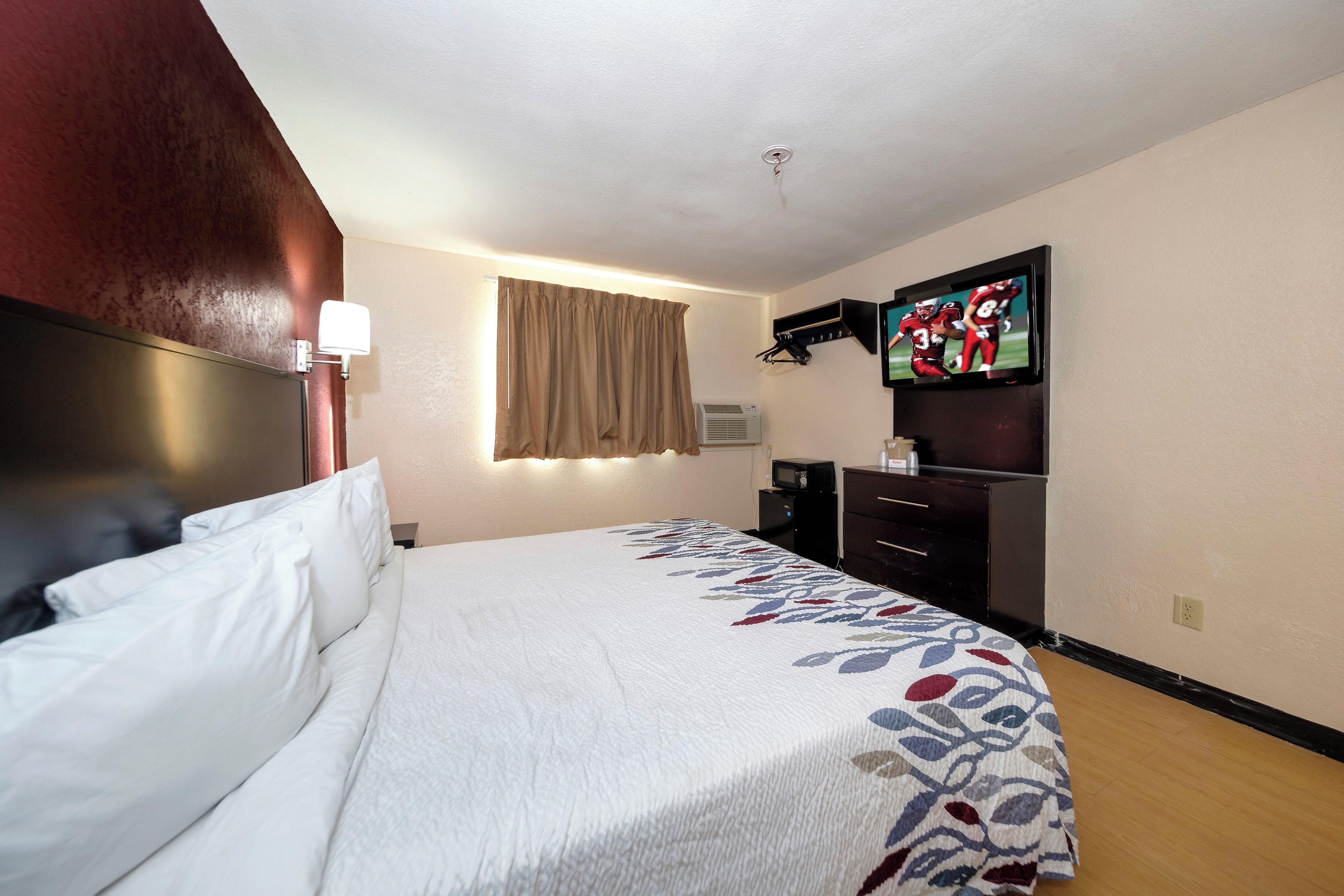 A hotel room with a bed, a television, a desk, and a wall-mounted air conditioning unit.