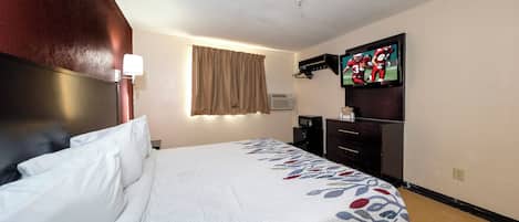 Una habitación de hotel con cama, televisor, escritorio y aire acondicionado instalado en la pared.