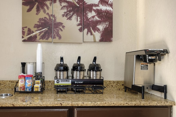 A coffee station with a Bunn coffee maker, a coffee dispenser, and a coffee machine. There are also paper cups and coffee creamer on the counter.