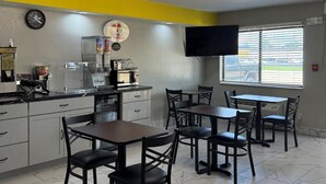 A restaurant with a counter, chairs, tables, a clock, a television, and a window with blinds. - Super 8 by Wyndham Evansville East (Evansville)