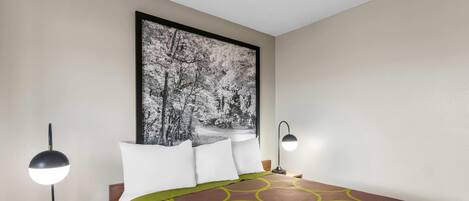 Habitación de hotel con cama, dos lámparas de noche, una mesita de noche y un cuadro grande en la pared.
