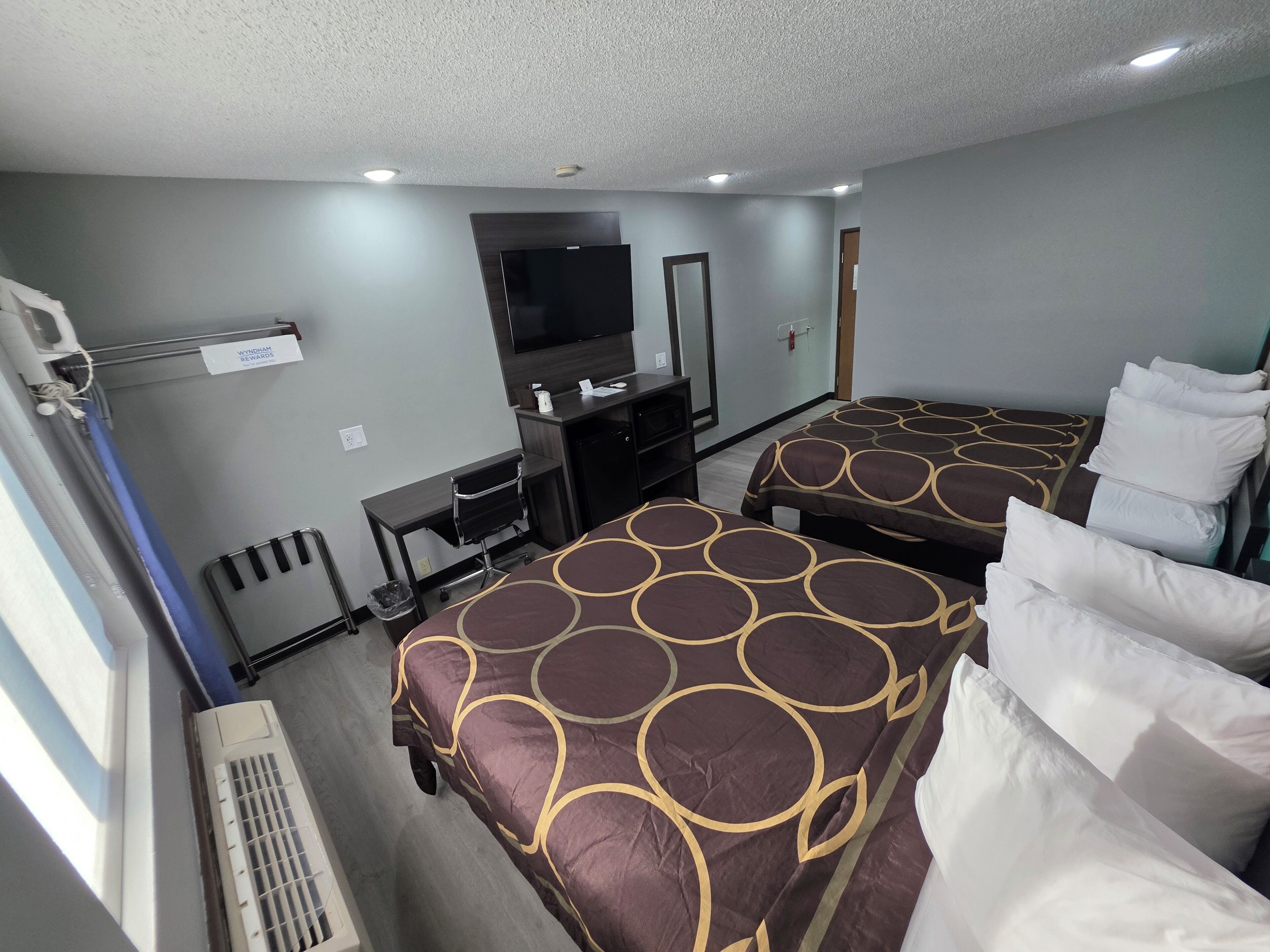 A hotel room with two beds, a desk, a television, and a window.
