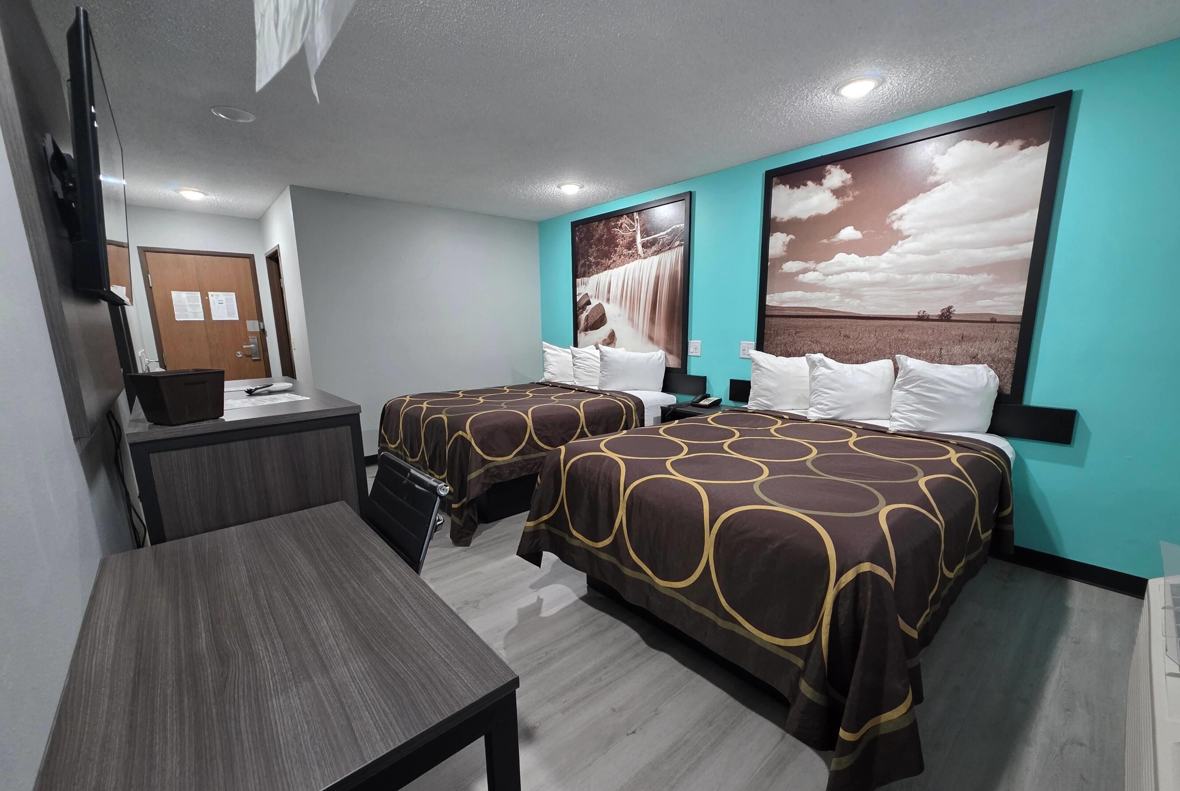 Habitación de hotel con dos camas, un escritorio, un televisor y obras de arte en las paredes.