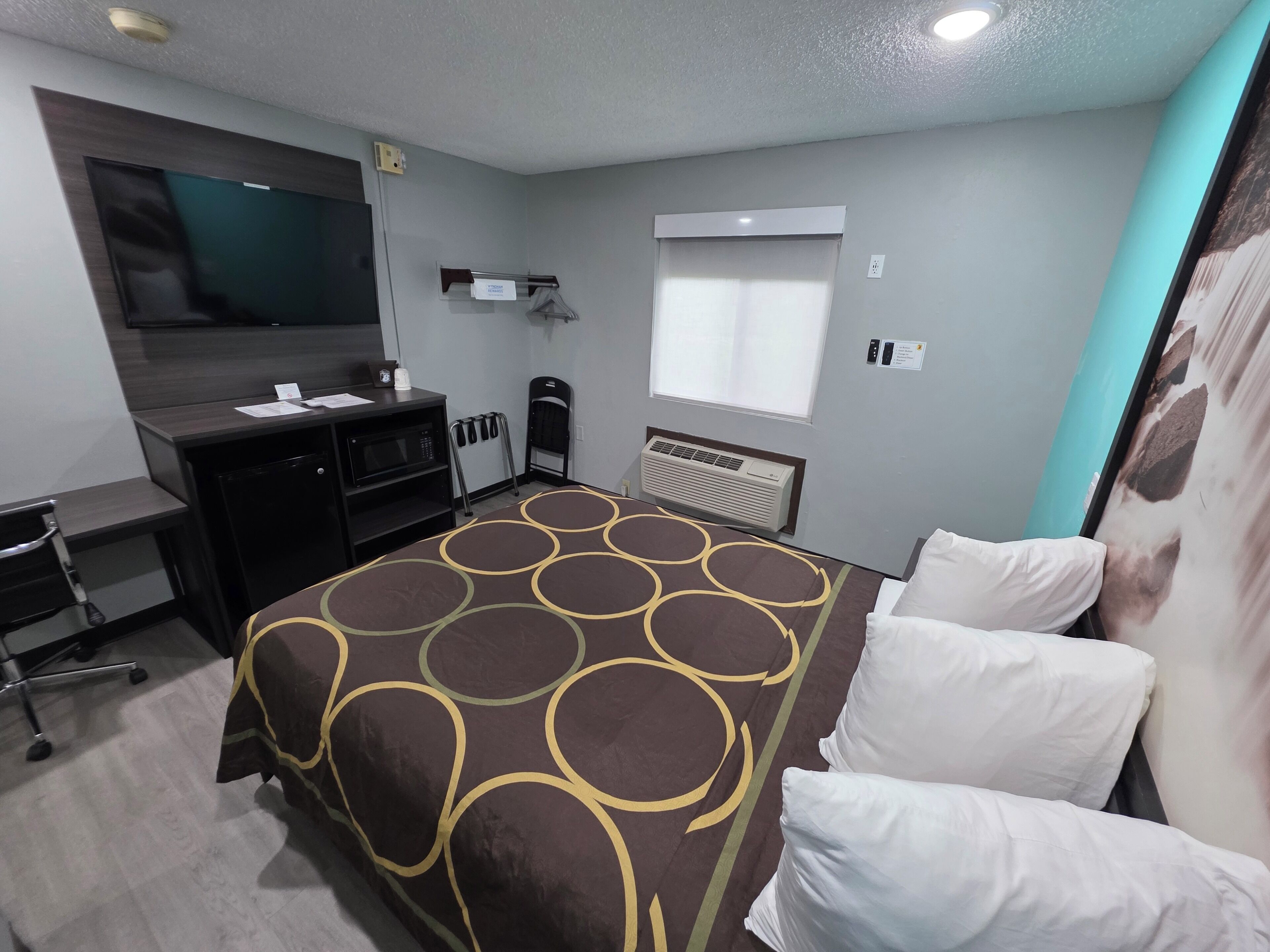 Une chambre d’hôtel équipée d’un lit, d’un bureau, d’une télévision, d’une fenêtre et d’un climatiseur fixé au mur.