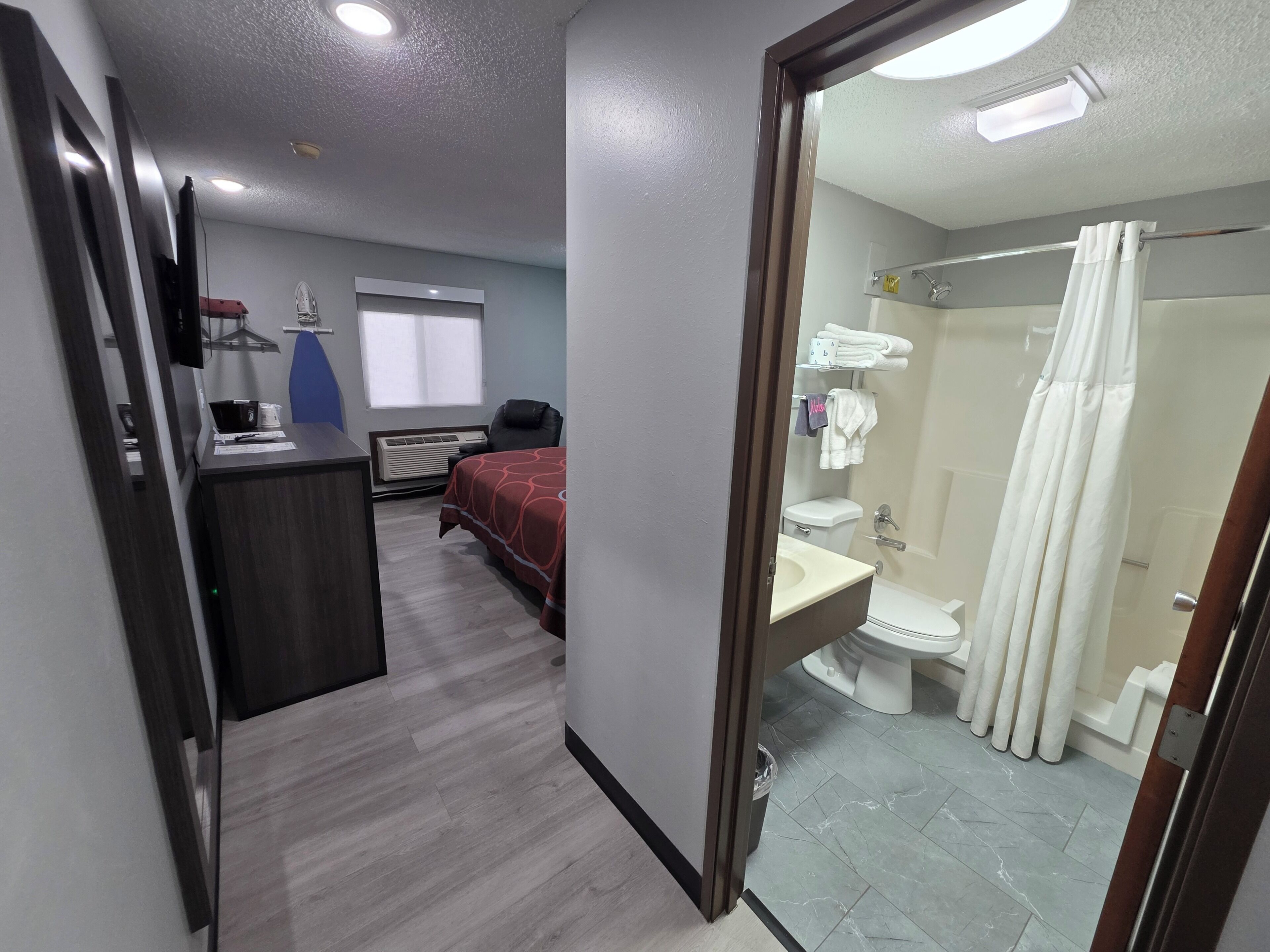 Hotelkamer met een bed, bureau, airconditioning en een badkamer met toilet, wastafel en douche.