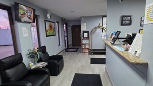 Aula, jossa on vastaanottotiski, mustat nahkaverhoillut istuimet, seinäkello ja seinälle asennettu televisio.