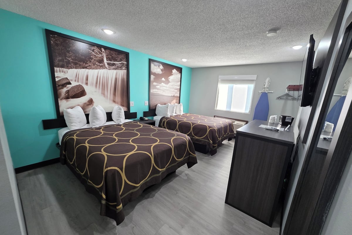 Une chambre d’hôtel avec deux lits, un bureau, un miroir et une grande fenêtre.