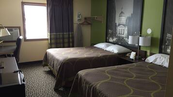 Quarto de hotel com duas camas, uma secretária, tábua de passar roupa, janela com cortinas e uma luminária na parede.