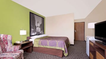 A hotel room with a bed, a chair, a desk with a lamp, a television, and a wall-mounted picture.