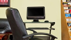 A workspace with a computer monitor on a stand, a keyboard, a mouse, and a leather chair.