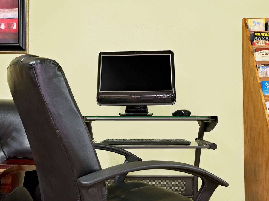 Et arbejdsområde med en computerskærm på en stander, et tastatur, en mus og en læderstol.