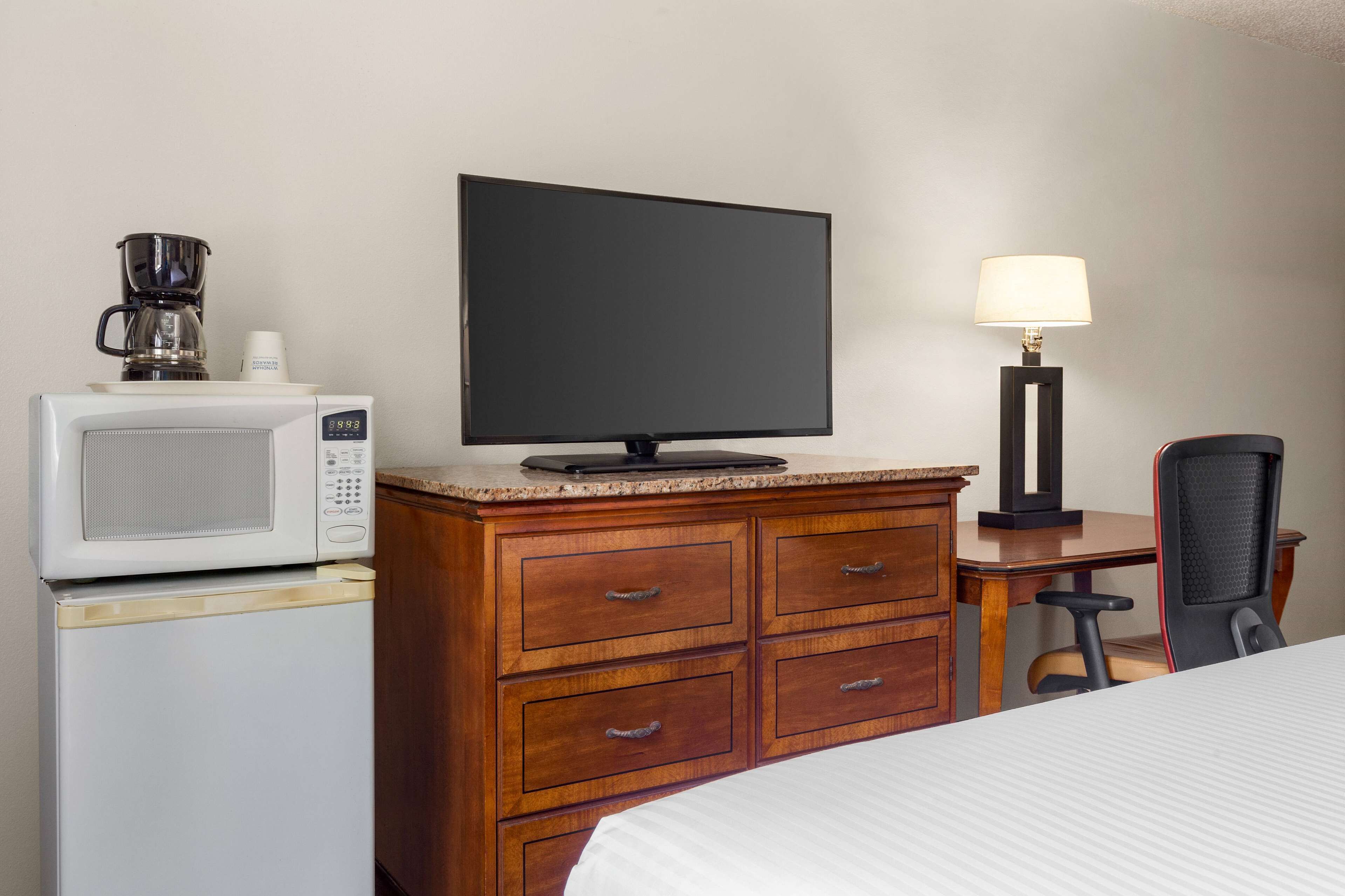 Ein Hotelzimmer mit Bett, Schreibtisch, Fernseher, Mikrowelle, Kaffeemaschine und Lampe.
