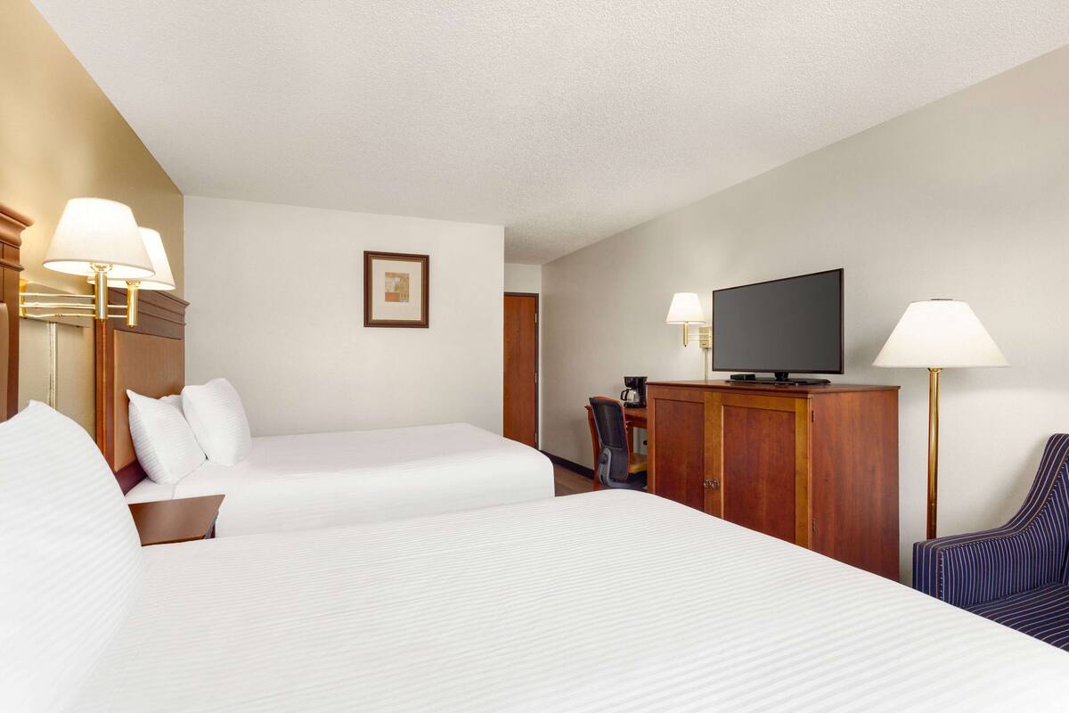 A hotel room with two beds, a television, a desk with a chair, and a lamp.