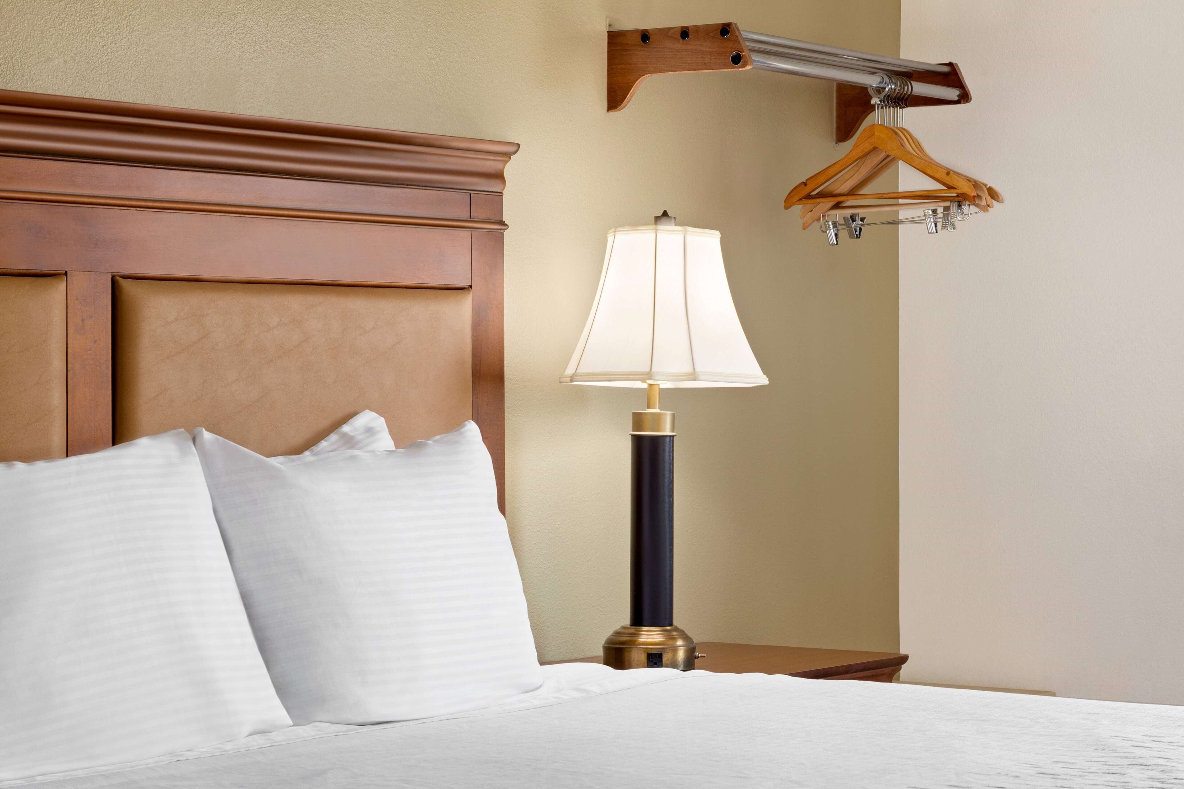 Une chambre d’hôtel avec une tête de lit en bois, une lampe de chevet et un porte-manteau en bois fixé au mur.