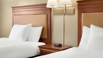 A hotel room with two beds, a nightstand, and two wall-mounted lamps.