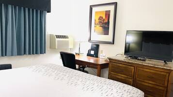 A hotel room with a bed, a desk, a chair, a television, a lamp, and a framed picture on the wall.