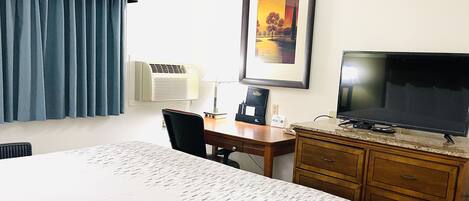 A hotel room with a bed, a desk, a chair, a television, a lamp, and a framed picture on the wall.