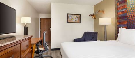 A hotel room with a bed, desk, chair, television, and artwork on the wall.