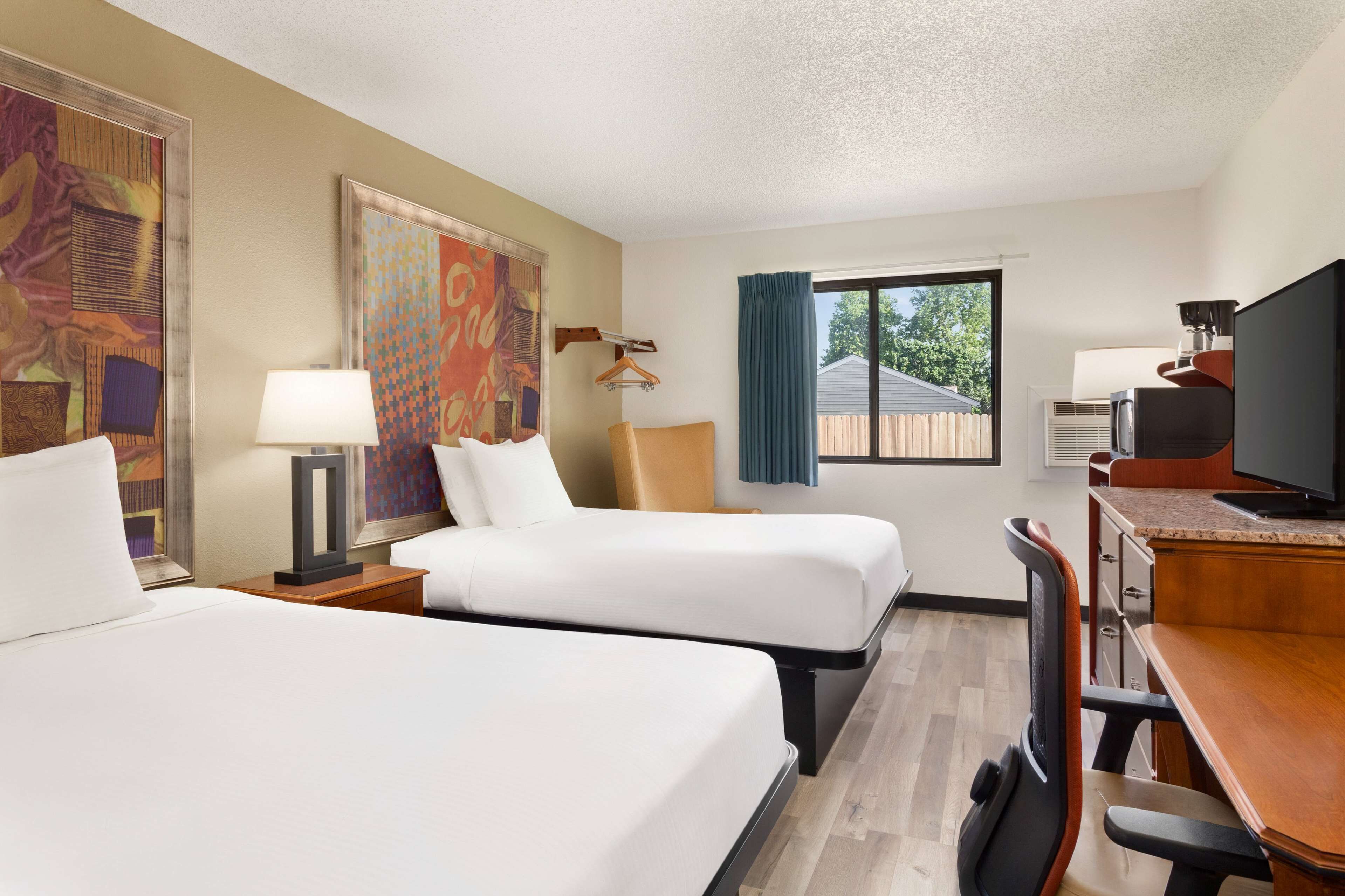 A hotel room with two beds, a desk with a television, a chair, and a window with a view of the outside.