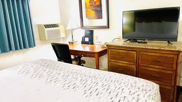 Een hotelkamer met een bed, een bureau met een computer, een televisie en een schilderij aan de muur.