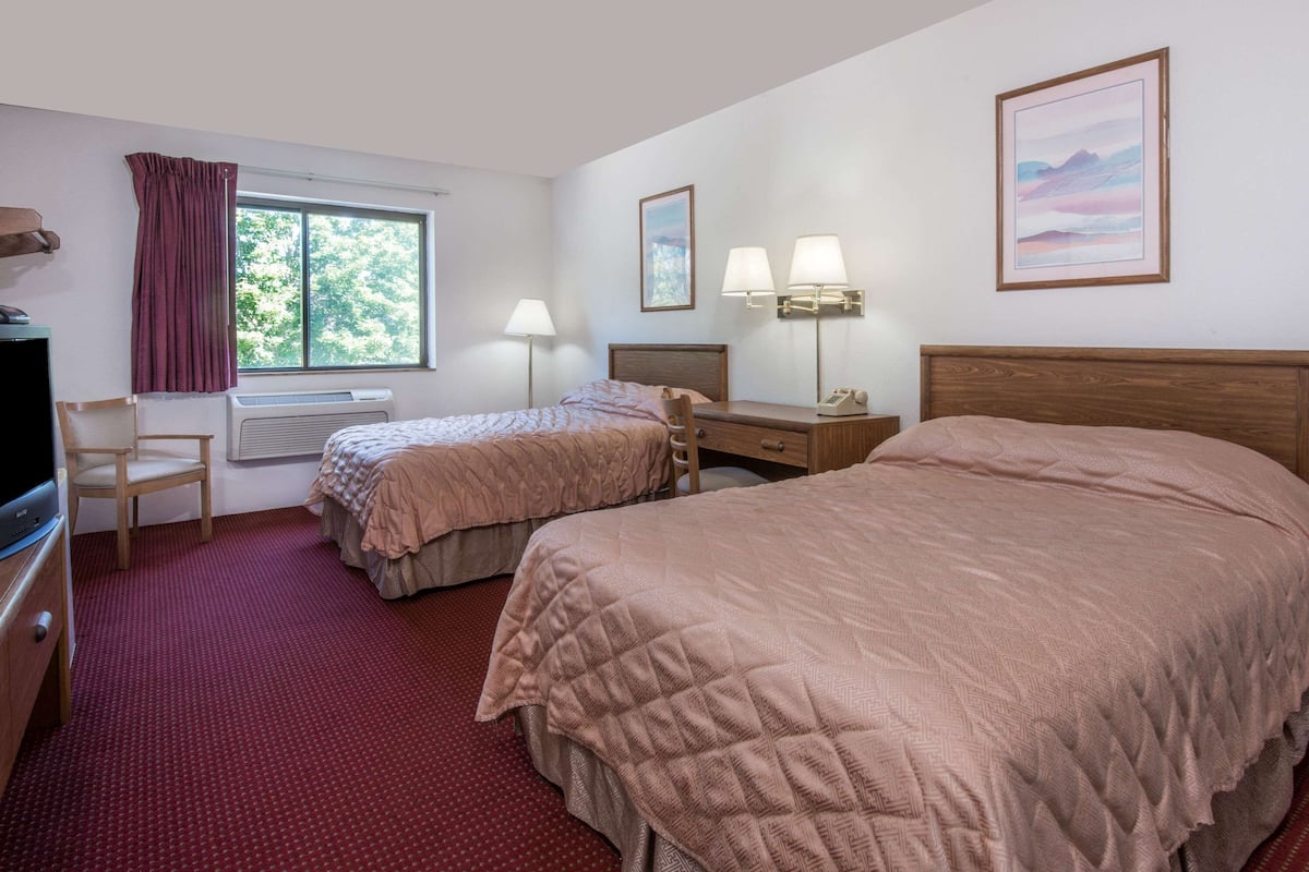 A hotel room with two beds, a desk, a chair, a TV, and a window with curtains.