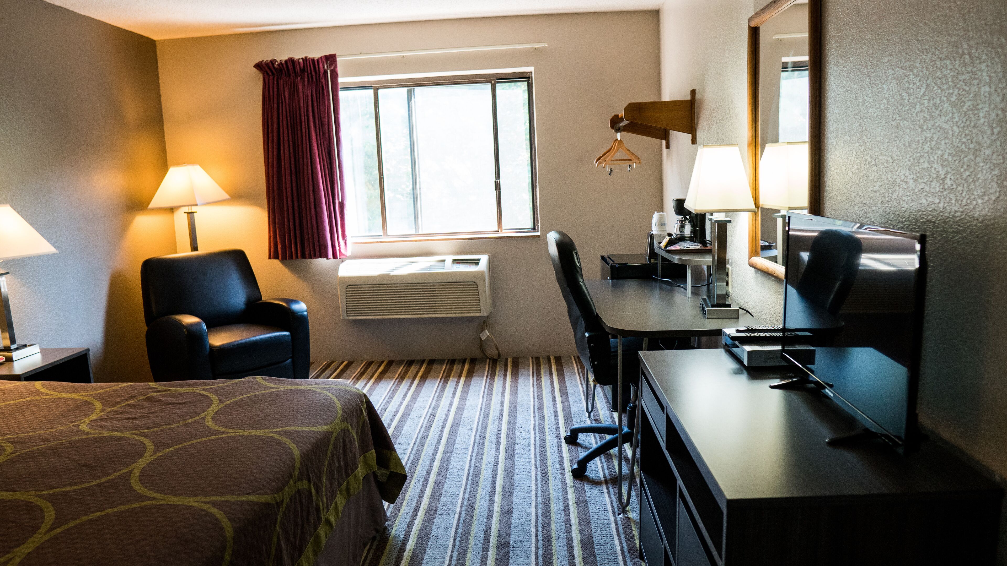 Una habitación de hotel con cama, escritorio, silla, televisión y ventana con cortinas.