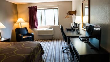 Una habitación de hotel con cama, escritorio, silla, televisión y ventana con cortinas.