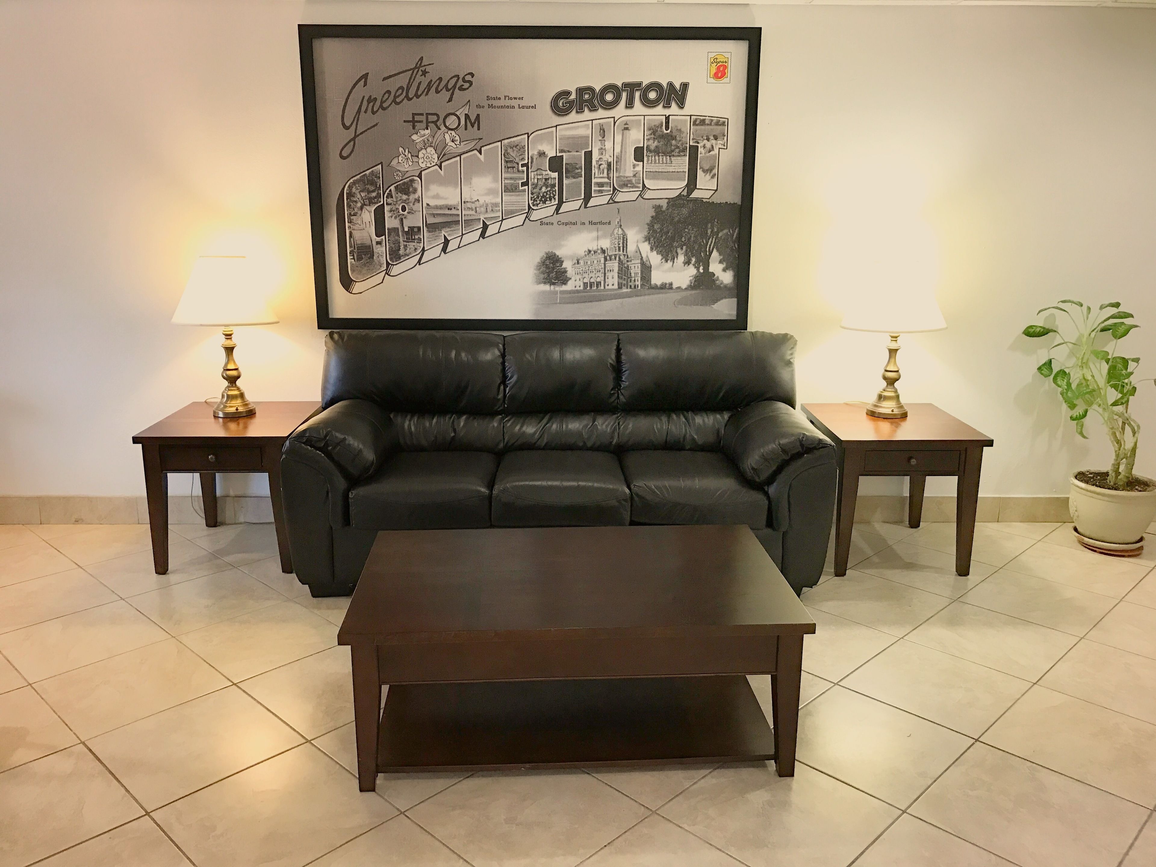 Ein Wohnzimmer mit einer schwarzen Ledersofa, zwei Beistelltischen mit Lampen, einem Couchtisch und einem gerahmten Bild von Groton, Connecticut.