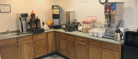 A breakfast area with a coffee machine, a fruit bowl, a refrigerator, and a clock on the wall.