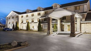 A multi-story hotel with a covered entrance, stone pillars, and a parking lot. - Super 8 by Wyndham Joliet I-55 N/Chicago (Joliet)