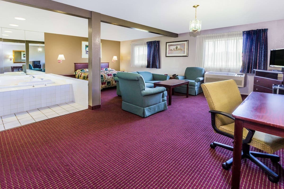 A hotel room with a large bed, a sitting area with a sofa and chairs, a small table, a desk with a computer, and a bathroom with a bathtub.