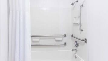 Baño blanco con bañera, barras de apoyo y cabezal de ducha.