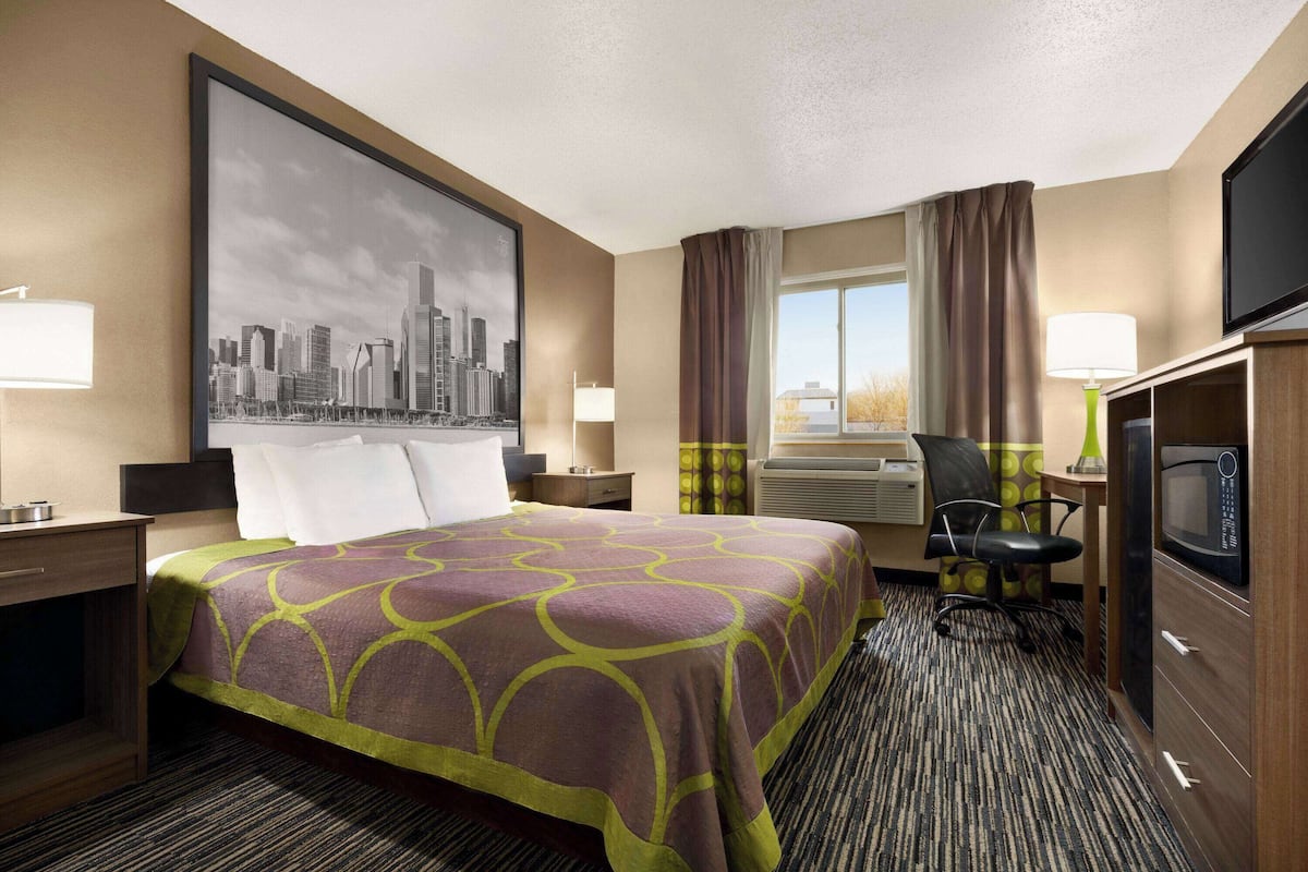 A hotel room with a large bed, a desk, a chair, a television, and a window with curtains.