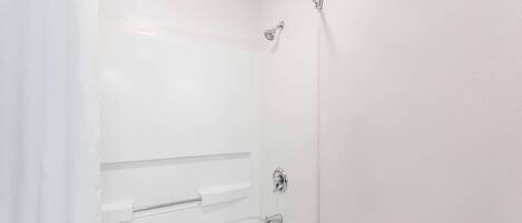 A white bathroom with a bathtub, a showerhead, and a towel rack.