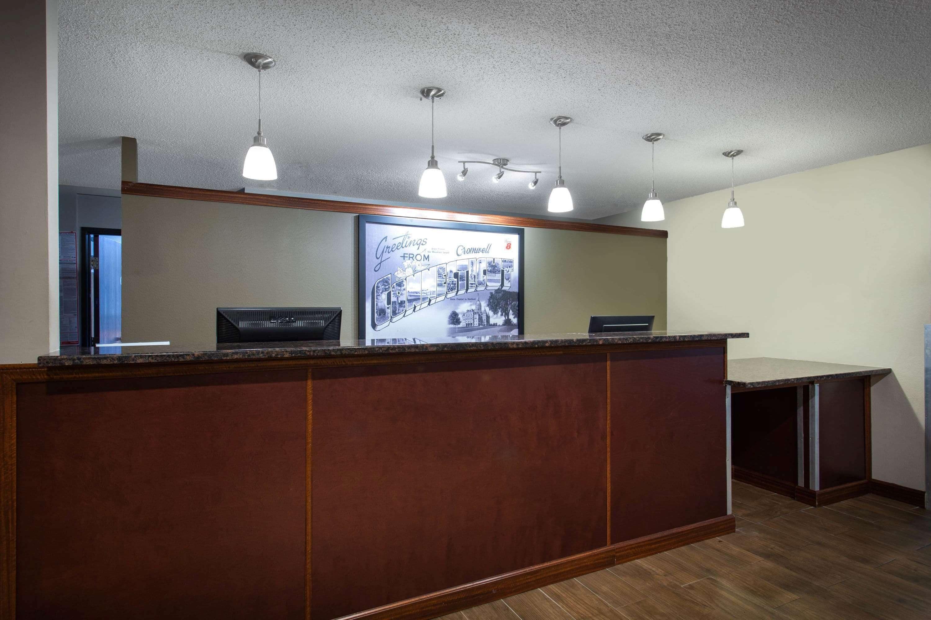 A reception desk with a wooden finish, overhead pendant lighting, and a framed welcome sign.