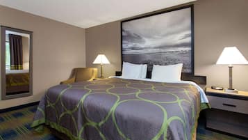 A hotel room with a large bed, two bedside lamps, a nightstand, a chair, and a large framed picture on the wall.
