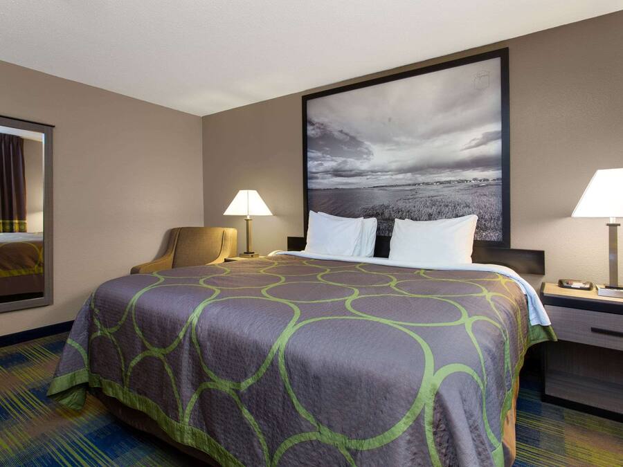 A hotel room with a large bed, two bedside lamps, a nightstand, a chair, and a large framed picture on the wall.