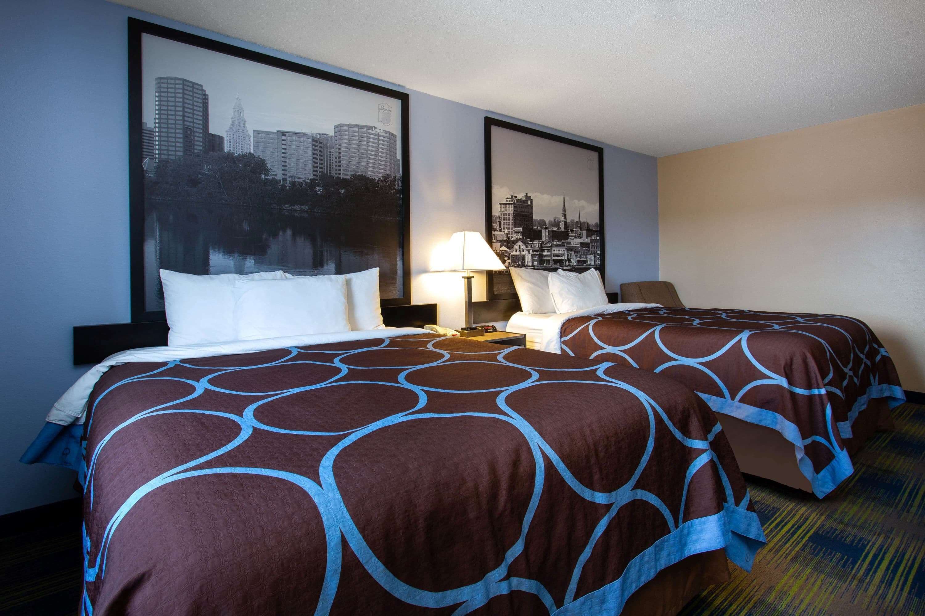 A hotel room with two beds, a cityscape view, and a lamp on the nightstand.