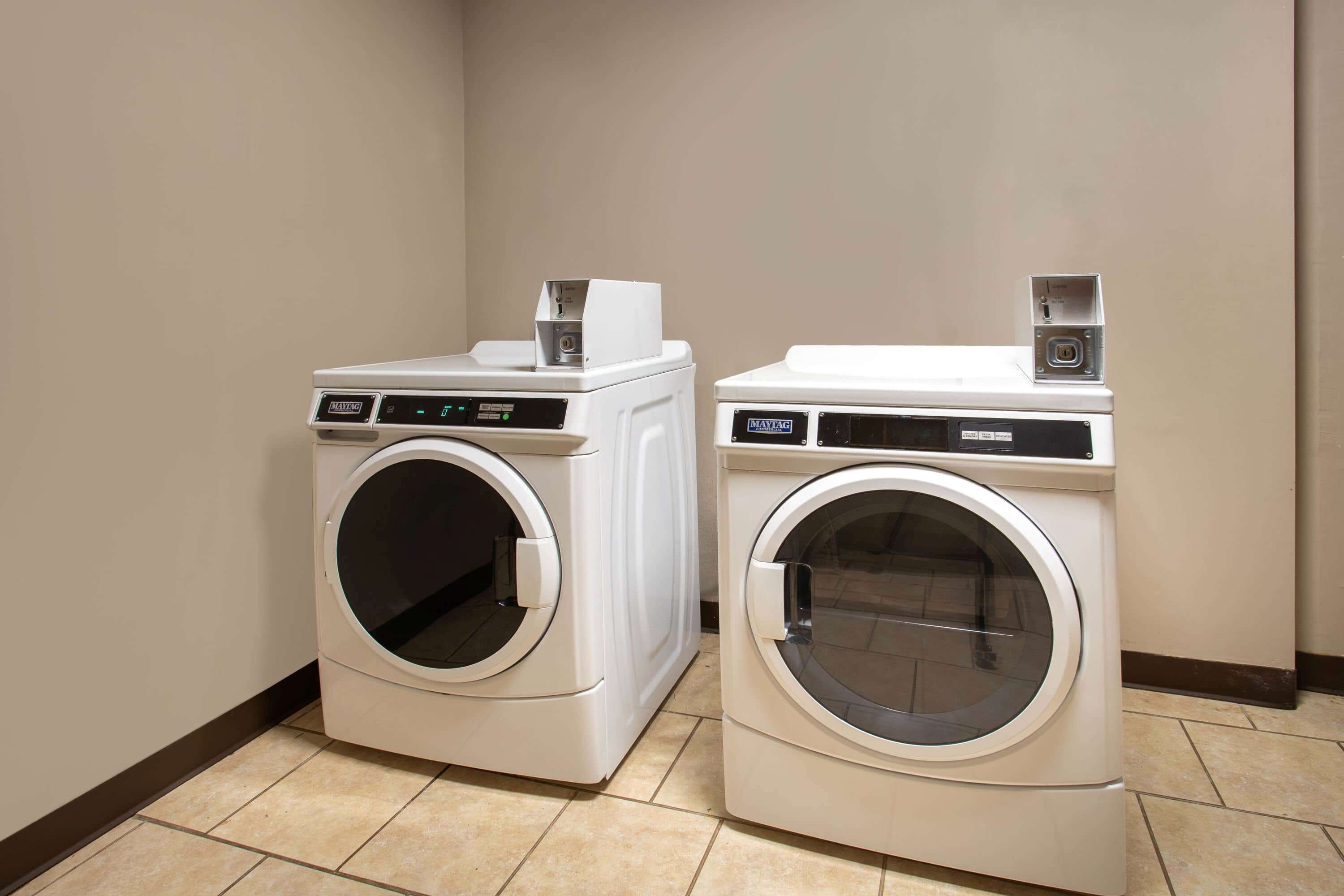 Two front-loading washing machines in a corner of a room with tiled flooring and plain walls.