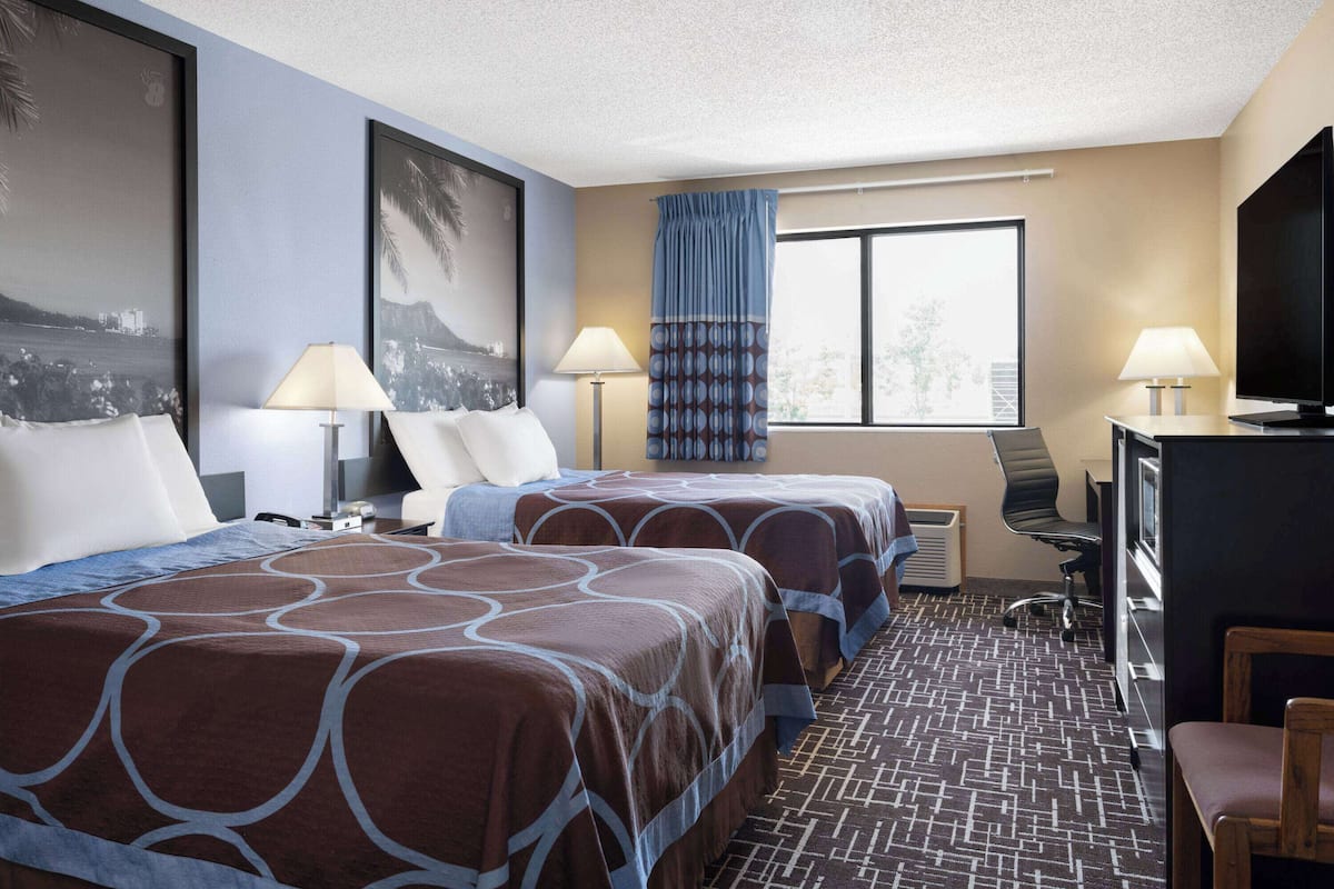 Une chambre d’hôtel avec deux lits, un bureau, une télévision et une fenêtre avec des rideaux.