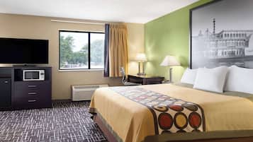 A hotel room with a bed, a flat-screen TV, a desk with a lamp, and a window with a curtain.