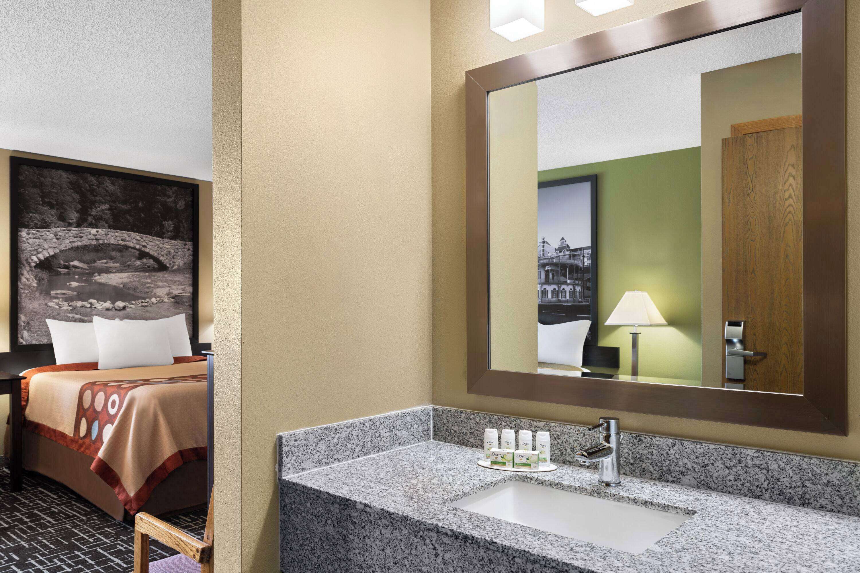 A hotel room with a bed, a bathroom with a granite countertop and sink, and a large mirror.