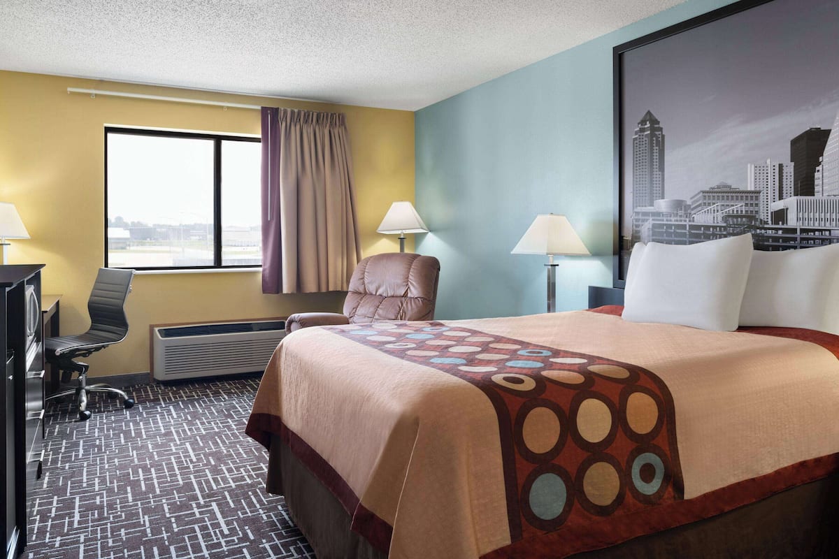 Une chambre d’hôtel avec un grand lit, deux chaises, un bureau et une fenêtre avec des rideaux.