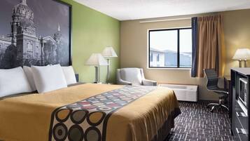 Una habitación de hotel con una cama grande, un escritorio, una silla y un ventanal con cortinas.